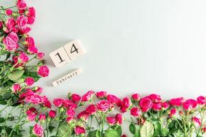 festive flower frame of mini pink roses and a wooden calendar with the date February 14. the concept of Valentine's Day. postcard. a copy space. photo