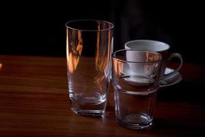 vasos de agua de vidrio transparente y tazas de café colocadas sobre una mesa de madera. foto