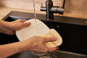 la mujer lava los platos con una esponja ecológica ecológica. concepto de cero residuos foto