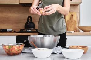 Woman in kitchen cooking a dough. Hands breaks an egg into a bowl photo