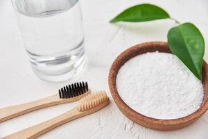 Bamboo toothbrushes, baking soda and glass of water on white background. photo