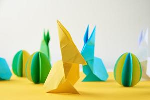 Paper origami Esater rabbits and colored eggs on a yellow background