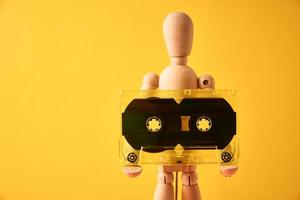 Wooden man hold retro cassette tape on yellow background photo