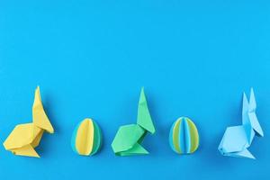 Paper origami Esater rabbits and colored eggs on blue background