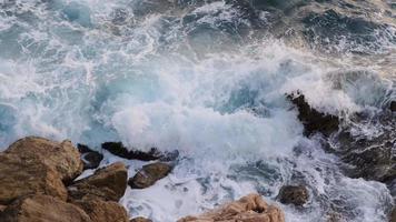 ondas do mar batendo e fluindo nas rochas costeiras ao pôr do sol, imagens da natureza 4k. video