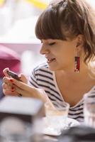 chica enviando mensajes de texto en el teléfono inteligente en la terraza de un restaurante con un fondo desenfocado foto