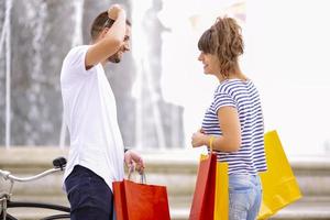 retrato de una alegre pareja joven caucásica hombre y mujer sosteniendo muchas bolsas de papel después de ir de compras mientras camina y habla en la calle. feliz pareja familiar con paquetes al aire libre. concepto de compra foto