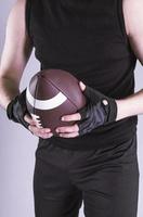 Young handsome American man holding rugby ball over isolated gray background photo
