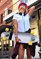 hermosa chica hipster con patineta con gafas de sol en la ciudad. foto