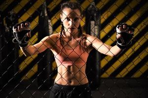 A female trainee of mixed martial arts warms up within the ring cage by stretching her back and legs. photo