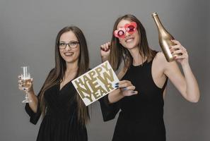 Two female friends celebrating New Year with confetti and champagne holding sign. isolated photo