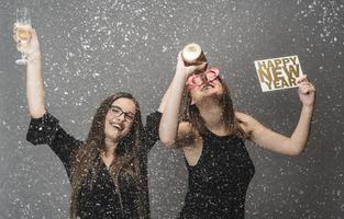 dos amigas celebrando el año nuevo con confeti y champán con cartel. aislado foto