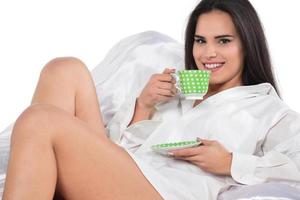 Cheerful tender female sitting with cup of coffee on be photo