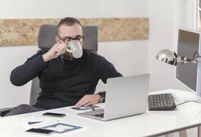 joven hombre de negocios que trabaja en casa con una computadora portátil y papeles en el escritorio foto