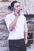 portrait of Young smiling handsome Asian man in semi formal suit using mobile phone photo