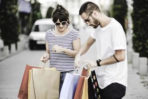 retrato de una alegre pareja joven caucásica hombre y mujer sosteniendo muchas bolsas de papel después de ir de compras mientras camina y habla en la calle. feliz pareja familiar con paquetes al aire libre. concepto de compra foto