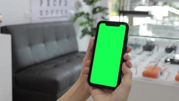 grüner bildschirm, grüner bildschirm des smartphones in der hand, verwenden sie den grünen bildschirm für die nahaufnahme des kopierraums. Chroma-Key-Modell auf dem Smartphone in der Hand. Frau hält Handy Greenscreen video