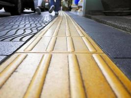 vista en perspectiva de ángulo bajo de peatones caminando con pavimentación táctil de guía ciega amarilla para discapacidad, y personas ciegas, textura en baldosas para discapacidad, enfoque selectivo, sendero foto