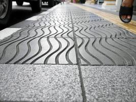 vista en perspectiva de ángulo bajo de peatones caminando con pavimentación táctil de guía ciega amarilla para discapacidad, y personas ciegas, textura en baldosas para discapacidad, enfoque selectivo, sendero foto