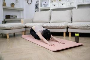 una joven asiática hace ejercicio en una alfombra de fitness, hace ejercicio en casa, un concepto de estilo de vida saludable foto