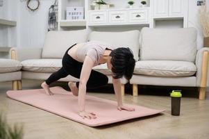 An Asian young woman is workout on fitness mat , exercise at home , healthy lifestyle concept photo
