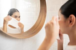 mujer joven limpiando y quitando maquillaje en la cara en el baño en casa, concepto de bienestar de belleza foto