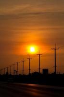 Atmósfera en el poste de alto voltaje de la tarde al lado de la carretera y el cielo anaranjado. El gran sol que se estaba poniendo era hermoso cuando estaba de camino a casa, era una hermosa atmósfera romántica. foto