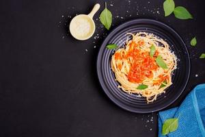 Delicious spaghetti pasta with prawns and cheese served on a black plate on a black background table Italian recipe, tomato sauce, vegetables, and spices top view with copy space photo