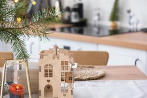 Key to the house on cozy home with Christmas decor on table of festive kitchen. Gift for New Year. Building, design, project, moving to new house, mortgage, rent and purchase real estate photo