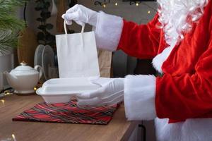 Food delivery to home service containers in hands of Santa Claus puts it on kitchen table and takes it away. Ready-made hot order, Christmas, New year holidays catering. photo