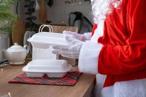 Food delivery to home service containers in hands of Santa Claus puts it on kitchen table and takes it away. Ready-made hot order, Christmas, New year holidays catering. photo