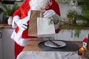 Santa Claus puts it on kitchen table and takes away paper bags with craft gift, homemade cakes and food delivery. Shopping, packaging recycling, handmade, delivery for Christmas and New year photo