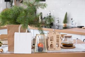 los paquetes de papel se burlan en la mesa servida en la cocina decorada para navidad. compras y regalos, presentes y comidas preparadas se entregan y preparan para el nuevo año foto