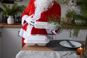 Food delivery to home service containers in hands of Santa Claus puts it on kitchen table and takes it away. Ready-made hot order, Christmas, New year holidays catering. photo