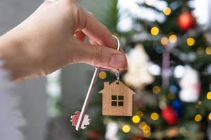 llave de la casa en la mano sobre el fondo del árbol de navidad. regalo para año nuevo, navidad. construcción, diseño, proyecto, mudanza a casa nueva, hipoteca, alquiler y compra de bienes inmuebles. copie el espacio foto