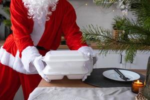 Food delivery to home service containers in hands of Santa Claus puts it on kitchen table and takes it away. Ready-made hot order, Christmas, New year holidays catering. photo