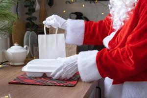 Food delivery to home service containers in hands of Santa Claus puts it on kitchen table and takes it away. Ready-made hot order, Christmas, New year holidays catering. photo