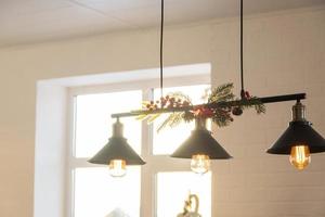 The black lampshade in the industrial loft style is decorated with spruce branches for Christmas and New Year on the background white brick wall. Close-up, minimalism photo