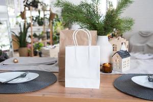 los paquetes de papel se burlan en la mesa servida en la cocina decorada para navidad. compras y regalos, presentes y comidas preparadas se entregan y preparan para el nuevo año foto