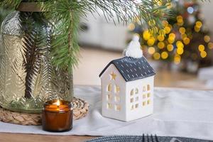 decoración navideña festiva en cocina blanca, desayuno festivo, interior escandinavo blanco. la figura de una casa acogedora en la mesa puesta. año nuevo, estado de ánimo, hogar acogedor. copie el espacio foto