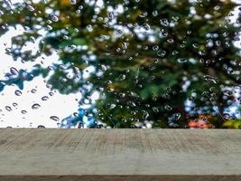 mesa de madera marrón, telón de fondo de gotas de lluvia sobre vidrio, desenfoque de naturaleza verde
