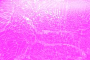 Defocus blurred transparent purple colored clear calm water surface texture with splashes and bubbles. Trendy abstract nature background. Water waves in sunlight with copy space. Pink water drop shine photo