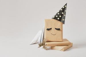 gift boxes with kraft paper on gray background, original gift decor with false eyelashes and party hat, minimalistic photo