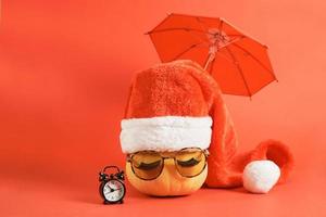 pumpkin with sunglasses and santa hat under an umbrella holidays in warm countries concept photo
