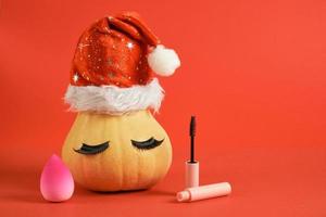 esponja de maquillaje rosa, rímel en empaque de maqueta rosa y calabaza en sombrero de santa y pestañas postizas foto