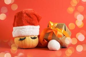 wrapped christmas gifts and pumpkin in santa hat and false eyelashes on red background photo