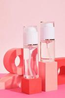 dos botellas de vidrio con spray y dispensador en un podio rosa sobre fondo rosa, botellas para perfume o suero foto