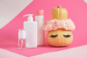 conjunto simulado de envases cosméticos y calabaza con diadema y pestañas postizas sobre fondo rosa foto