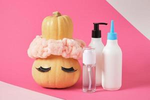 conjunto simulado de envases cosméticos y calabaza con diadema y pestañas postizas sobre fondo rosa foto