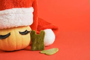 gau sha scrapers made of jadeite and a cute pumpkin with eyelashes and a santa hat on red background photo